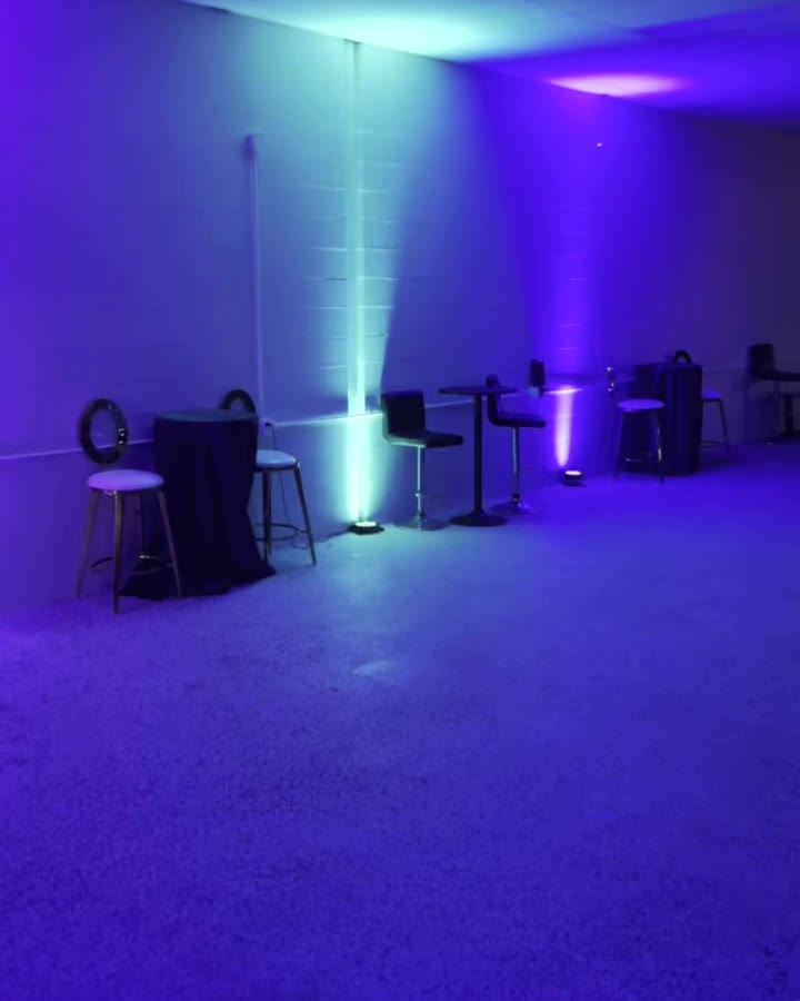 Lounge corner with high-top tables and bar stools under colored uplights