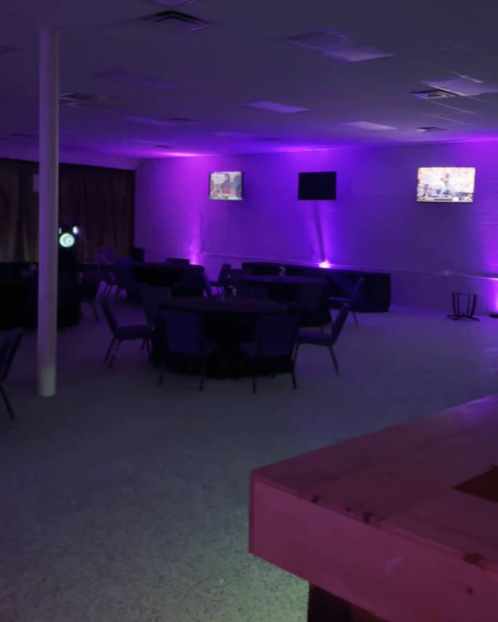 Purple uplighting and wall-mounted TVs along the side of the hall