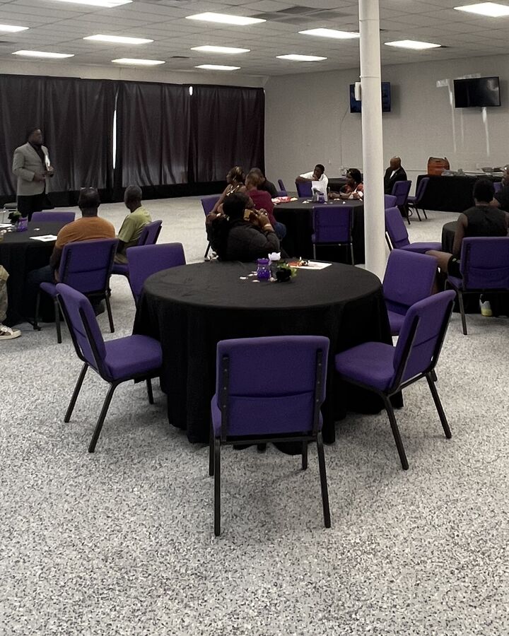 Guests seated at round tables with black linens and purple chairs during a daytime event at the EBE Center