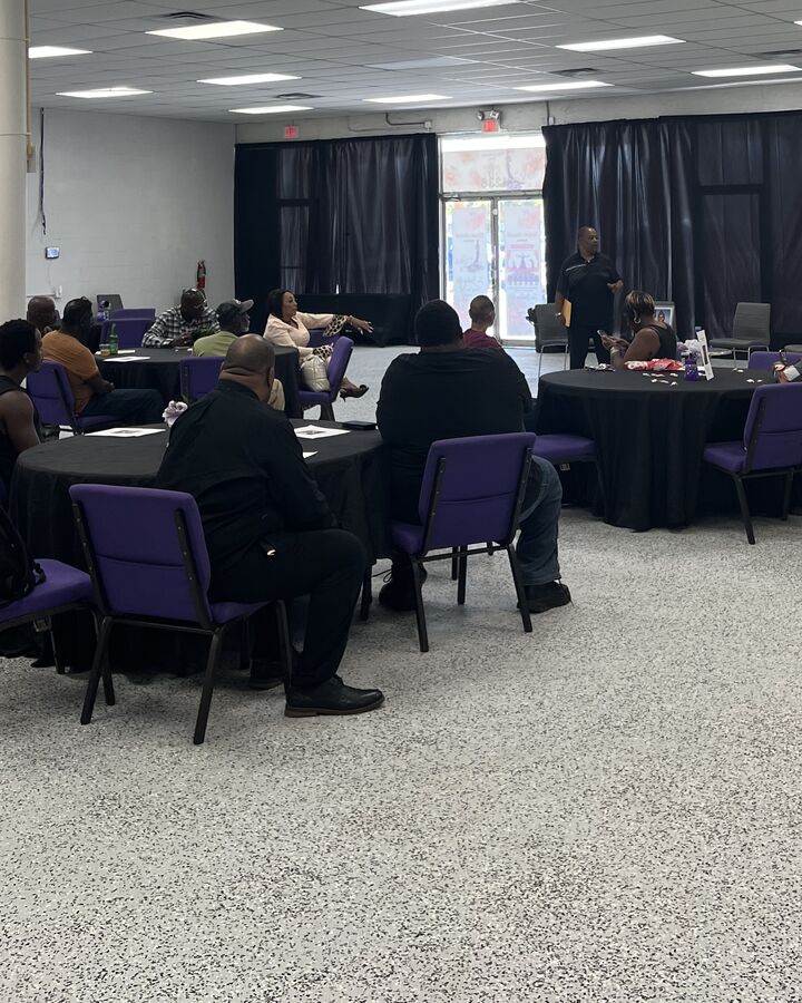Guests at round tables facing a speaker near the front doors of the EBE Center
